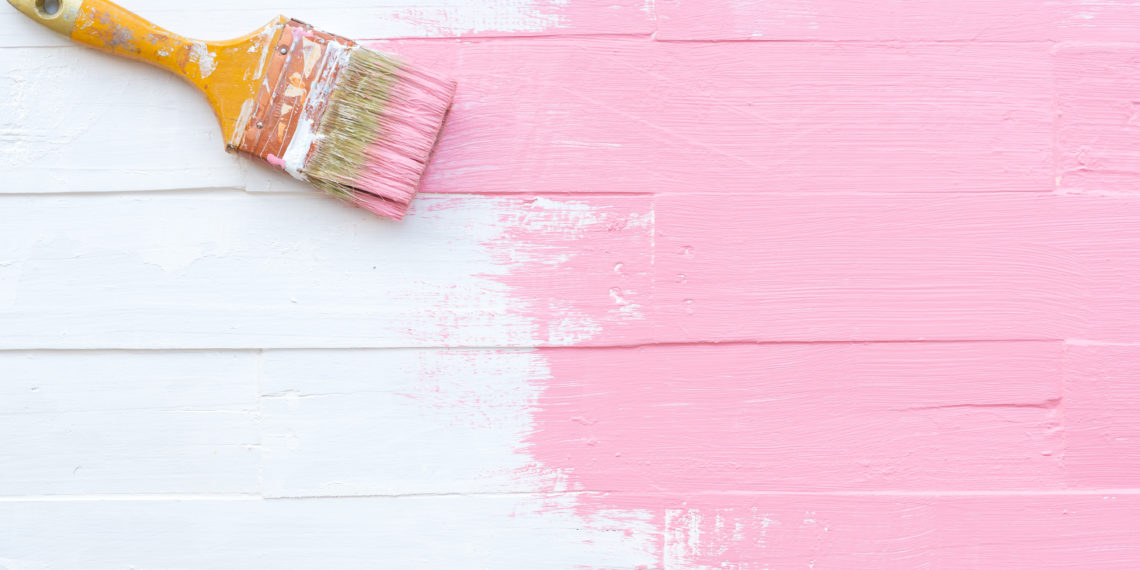 Close up paintbrush painting pink color on a white wooden table
