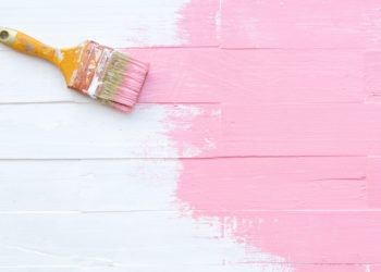Close up paintbrush painting pink color on a white wooden table