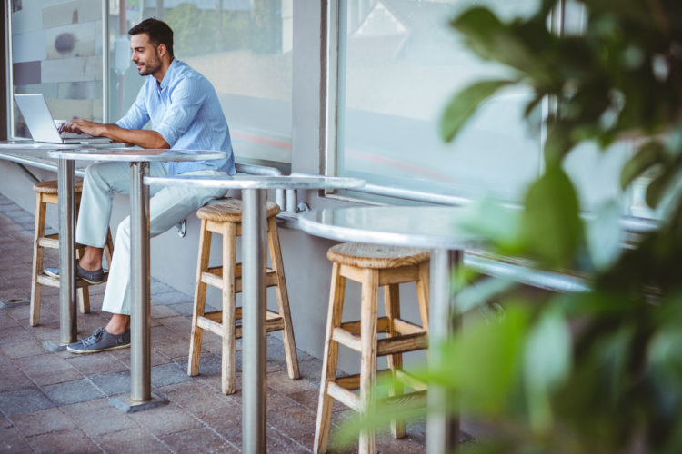 Distant view of a smiling businessman using his laptop outside a cafe