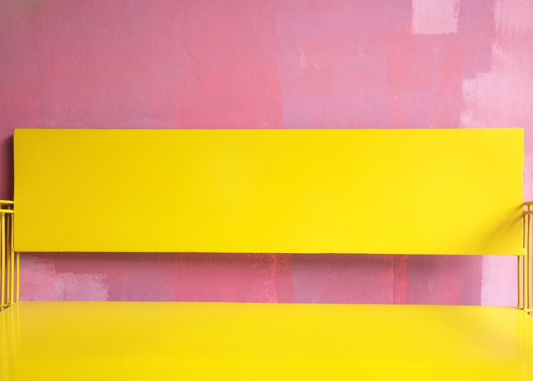 Vintage bright yellow Bench Against grunge pink painted Wall, bright summer colour