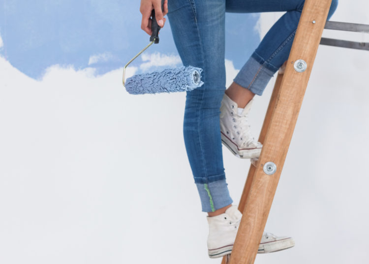 Woman holding paint roller on ladder against half painted wall