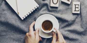 Woman hands holding tasty coffee espresso in small cup on grey plaid. Home concept. Top View.