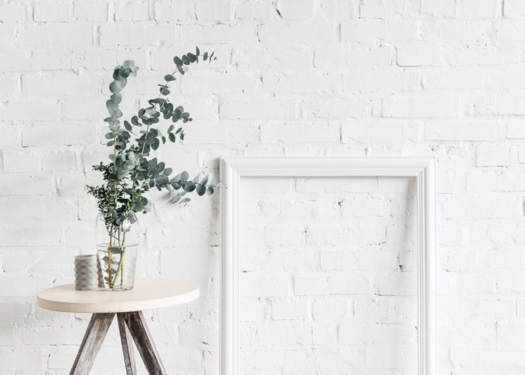 empty frame in front of white brick wall with flower pot on table, mockup concept