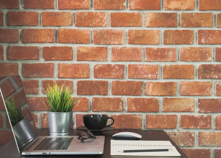 Desk of work table on brick wall background in office with laptop computer , notebook , calculator and a cup of coffee for creative marketing plan to success planning of company