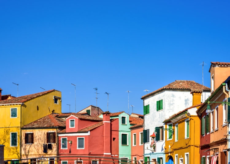 Daylight view to colorful buildings facades with chimney and antennas on rooftop. Bright blue clear sky. Negative copy space, place for text. Burano, Italy