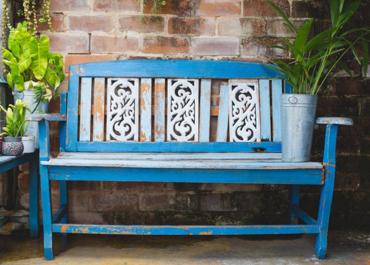 Blue wooden bench in flower garden with brick wall