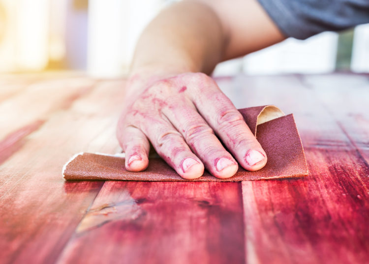 hand sanding and smoothing red wooden with sandpaper.