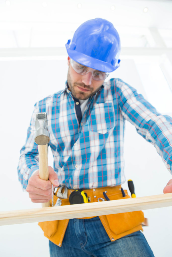 Low angle view of carpenter hitting nail on wooden plank at home