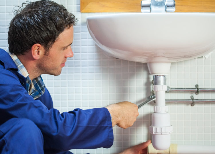 Handsome happy plumber repairing sink in public bathroom