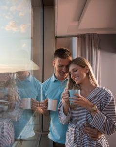 romantic happy young couple enjoying evening coffee and beautiful sunset landscape of the city while standing by the window