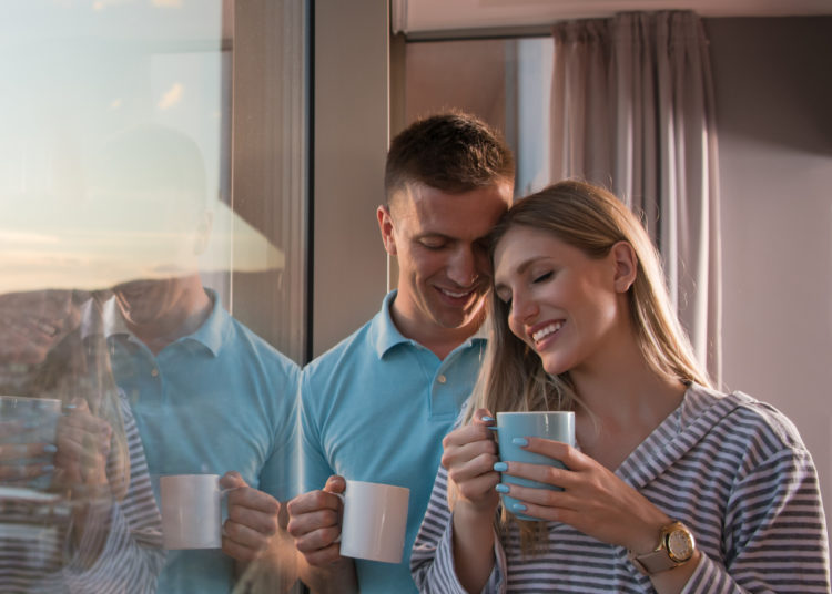 romantic happy young couple enjoying evening coffee and beautiful sunset landscape of the city while standing by the window