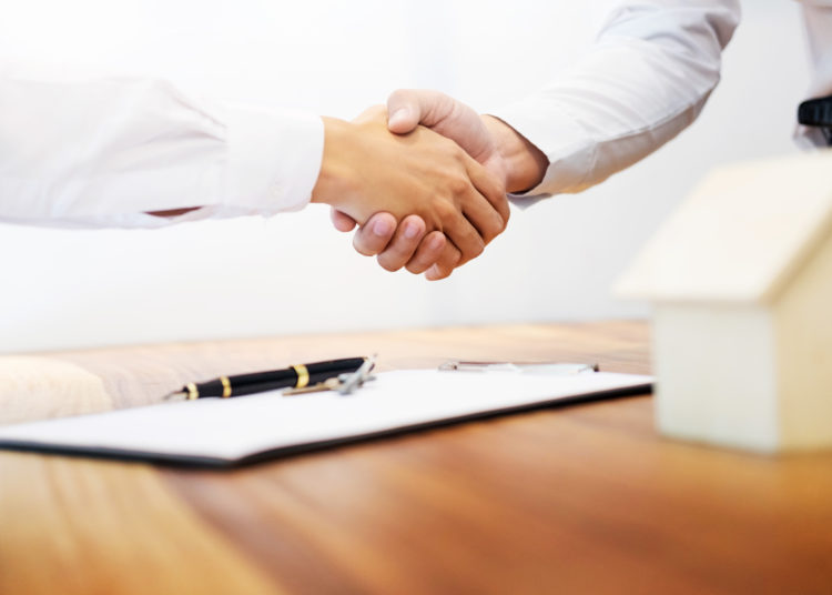 Estate agent shaking hands with customer after contract signature as successful agreement in real estate agency office. Concept of housing purchase and insurance.