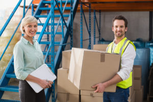 Worker holding box with manager holding clipboard in a large warehouse