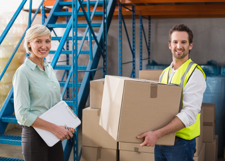 Worker holding box with manager holding clipboard in a large warehouse