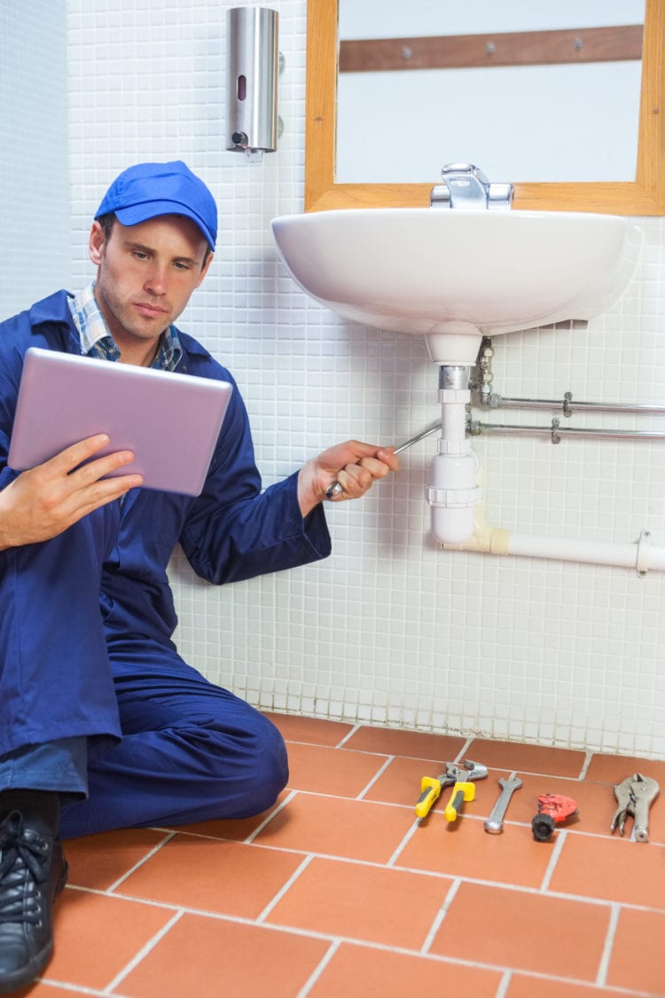 Focused plumber consulting tablet in public bathroom