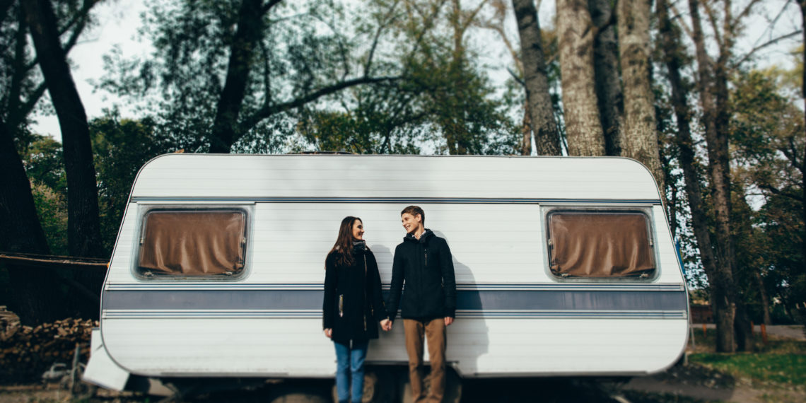 Couple in love holding hands and looking at each other and smiling. Couple in love walking near camper
