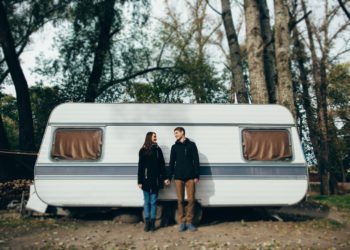 Couple in love holding hands and looking at each other and smiling. Couple in love walking near camper