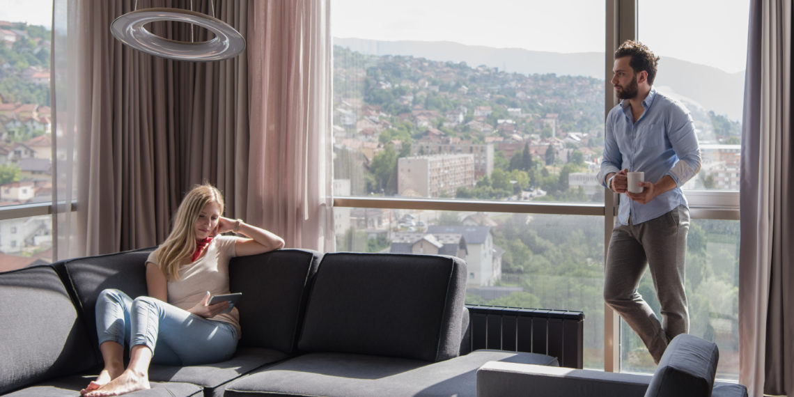 Young couple relaxing at home using tablet computer reading in the living room near the window on the sofa couch.