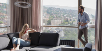 Young couple relaxing at home using tablet computer reading in the living room near the window on the sofa couch.