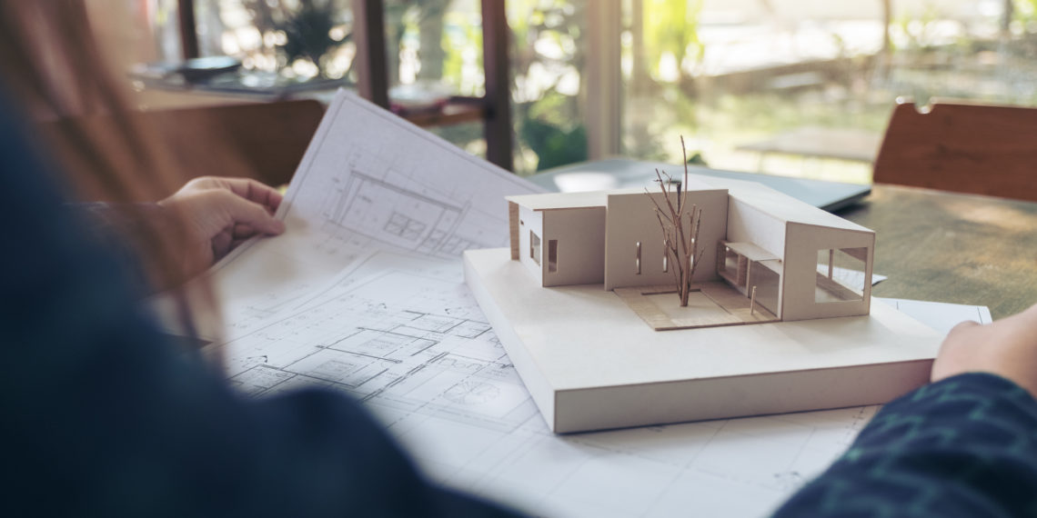 An architect working and looking at an architecture model with shop drawing paper on table
