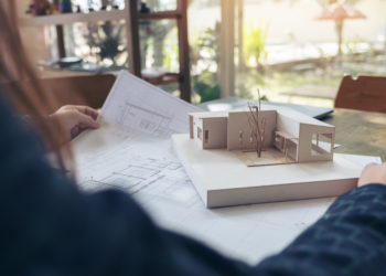 An architect working and looking at an architecture model with shop drawing paper on table