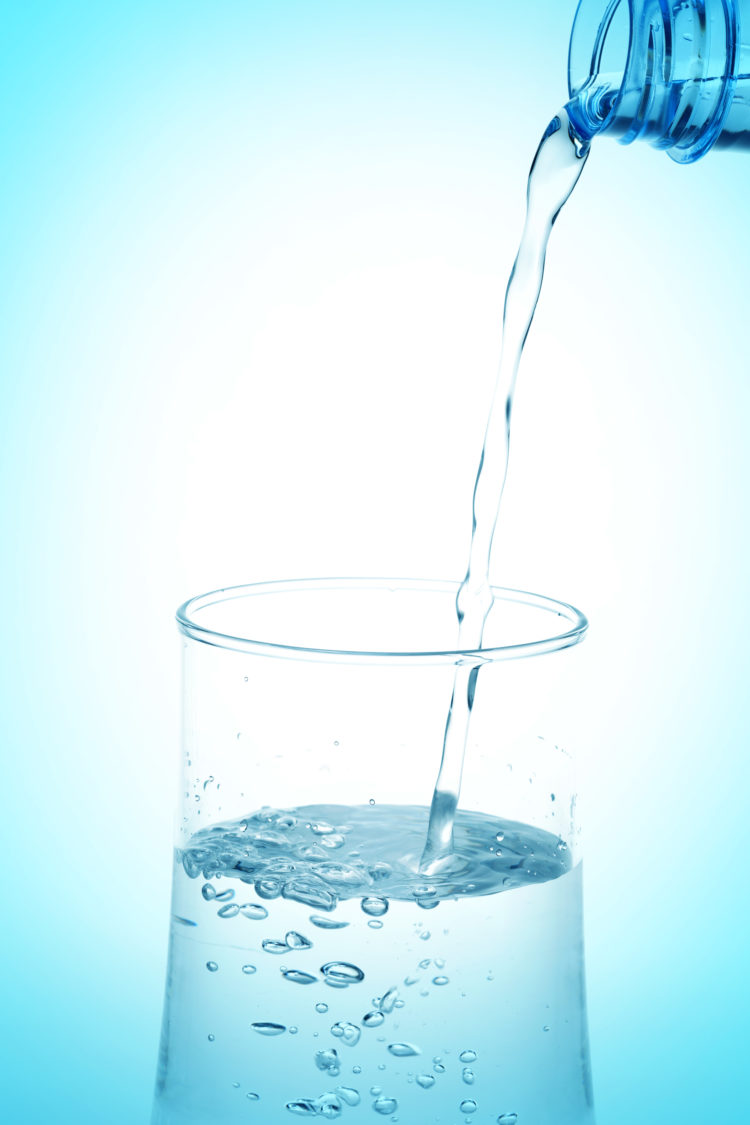 Pouring water from bottle into glass on white background