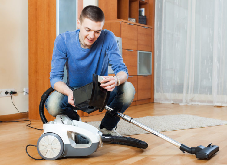 Smiling man vacuuming with vacuum cleaner on parquet floor in living room