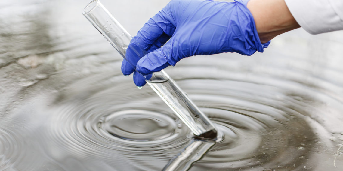 Researcher holds a test tube with water in a hand in blue glove