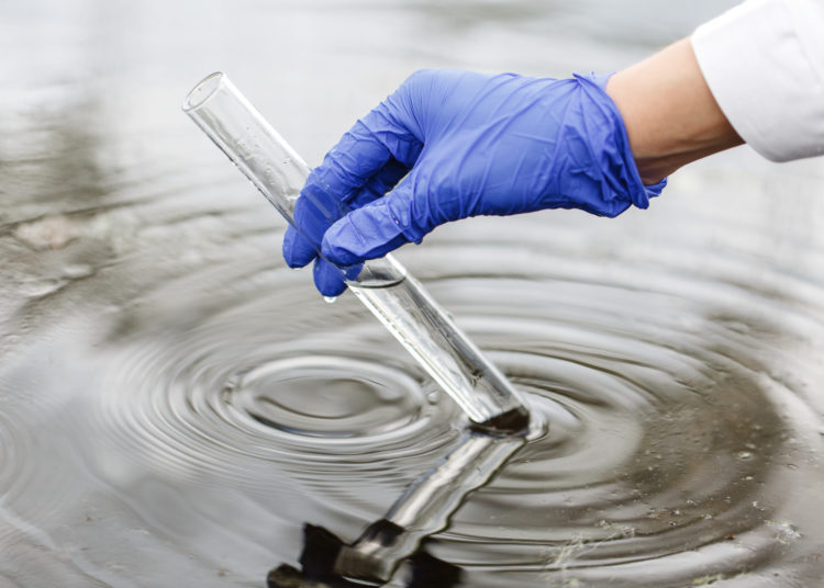 Researcher holds a test tube with water in a hand in blue glove