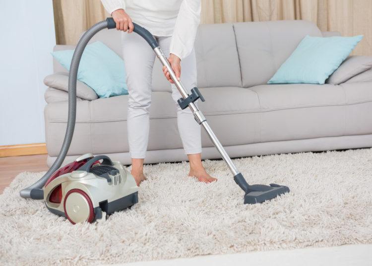 Woman using vacuum cleaner on rug at home in the living room