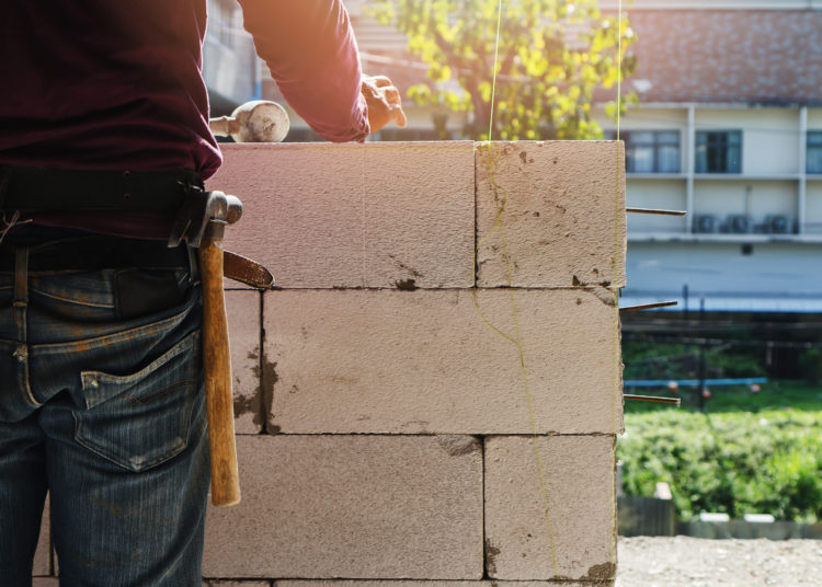 Mason worker building exterior walls, Industrial bricklayer installing bricks on construction site