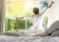 man happy waking up in the bed rising hands to window in the morning with fresh feeling relax
