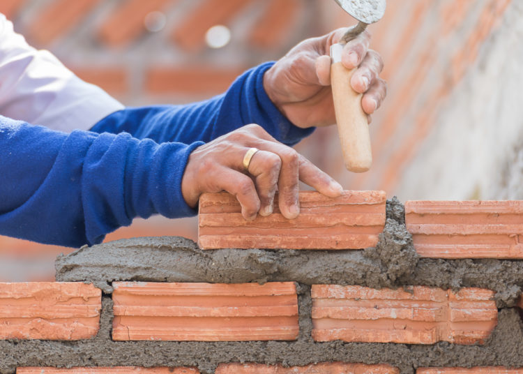 Bricklayer working in construction site of a brick wall. Bricklayer putting down another row of bricks in site