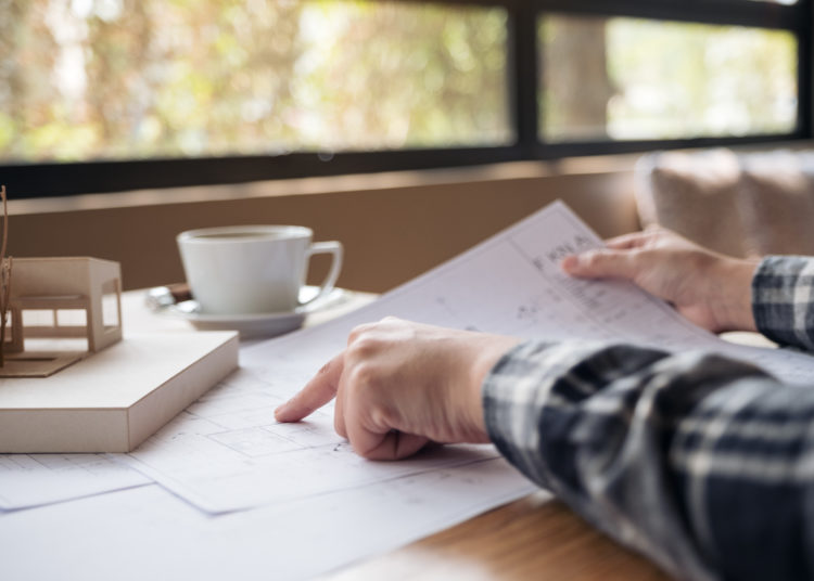 An architect working on an architecture model with shop drawing paper and coffee cup on table