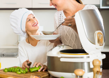 Happy 25-30 years old mother and little daughter using multicooker at kitchen