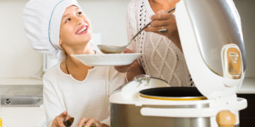 Happy 25-30 years old mother and little daughter using multicooker at kitchen