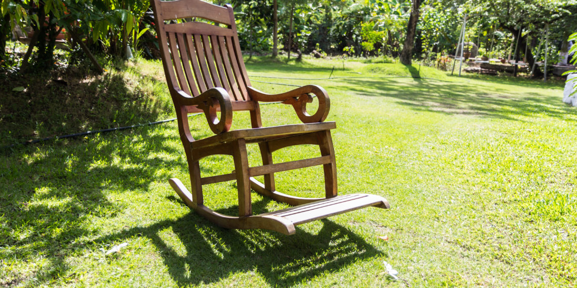 Empty rocking chair over grass at summer sunset