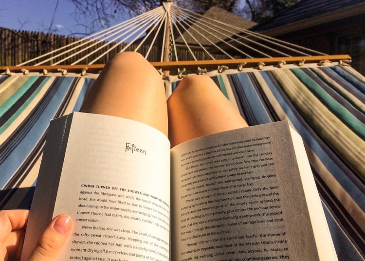 Young woman reading a book lying on hammock on the patio