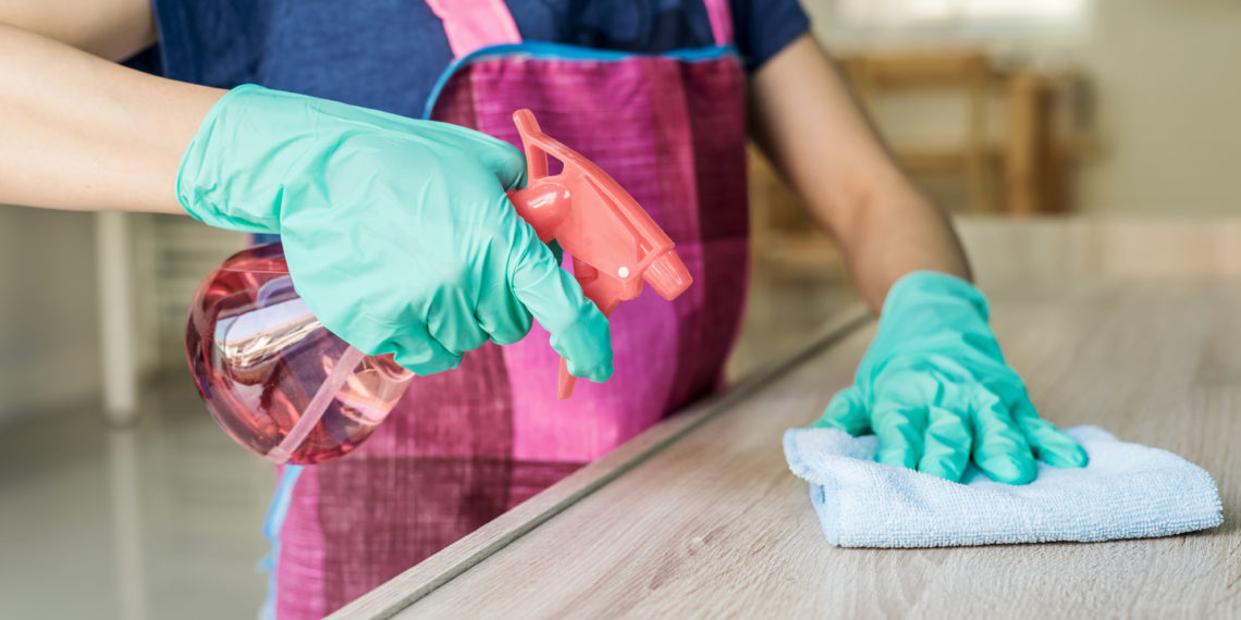 Young woman in protective gloves using a duster and spray for cleaning furniture