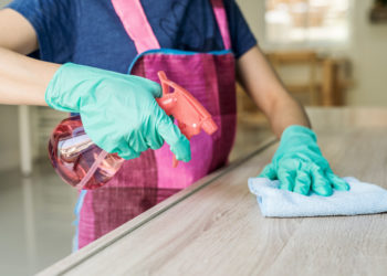 Young woman in protective gloves using a duster and spray for cleaning furniture