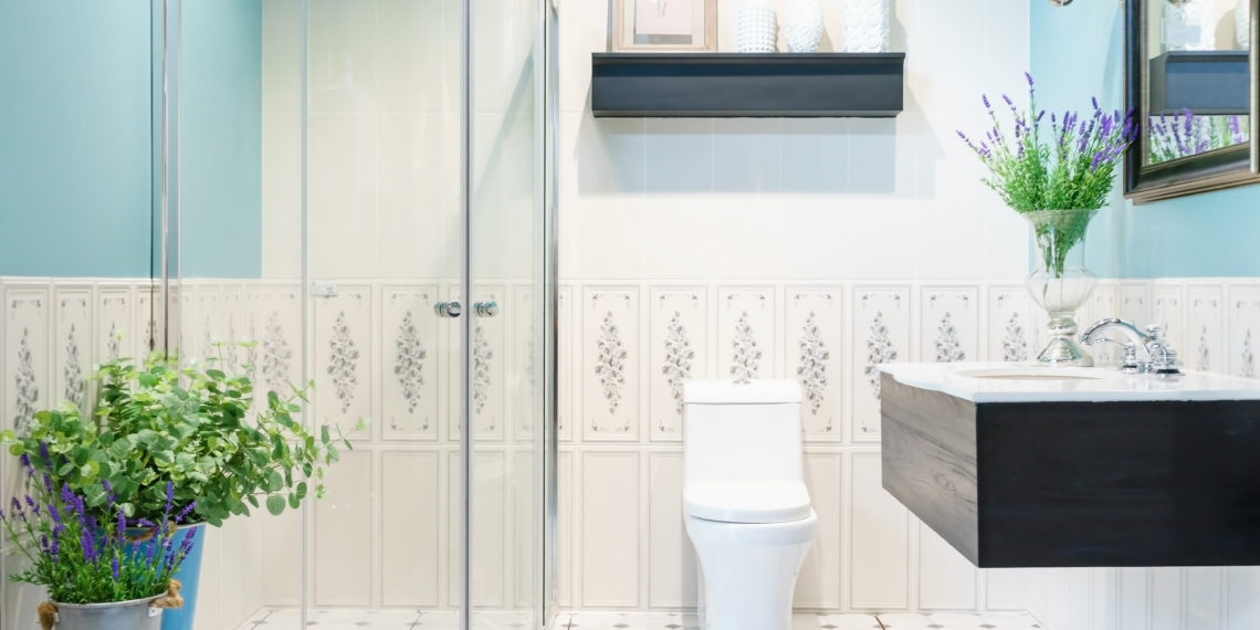 Modern spacious bathroom with bright tiles with glass shower, toilet and sink. Side view