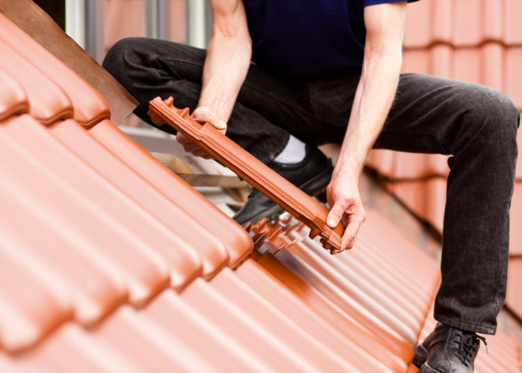 Roofing - construction worker standing on a roof covering it with tiles