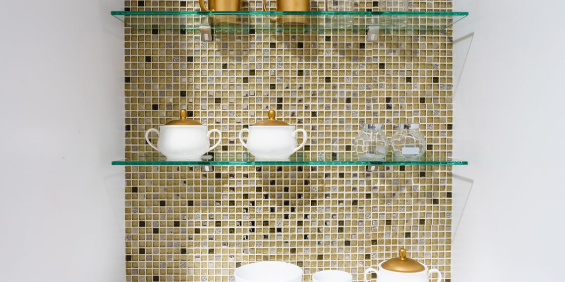 kitchen ceramic and white mug on a glass shelves in a white cabinet with colorful mosaic background.