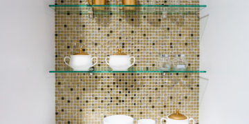 kitchen ceramic and white mug on a glass shelves in a white cabinet with colorful mosaic background.