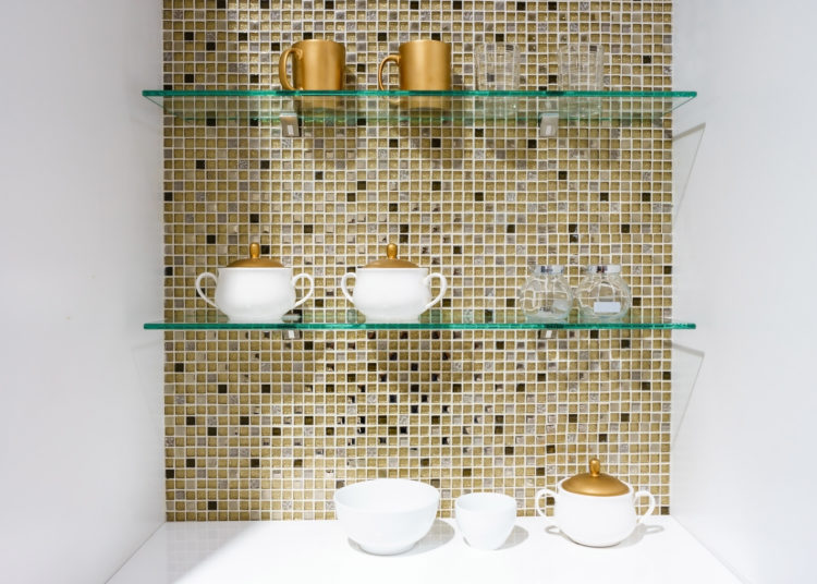 kitchen ceramic and white mug on a glass shelves in a white cabinet with colorful mosaic background.