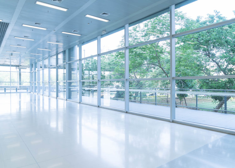 Blurred abstract background interior view looking out toward to empty office lobby and entrance doors and glass curtain wall with frame - blue white balance processing style