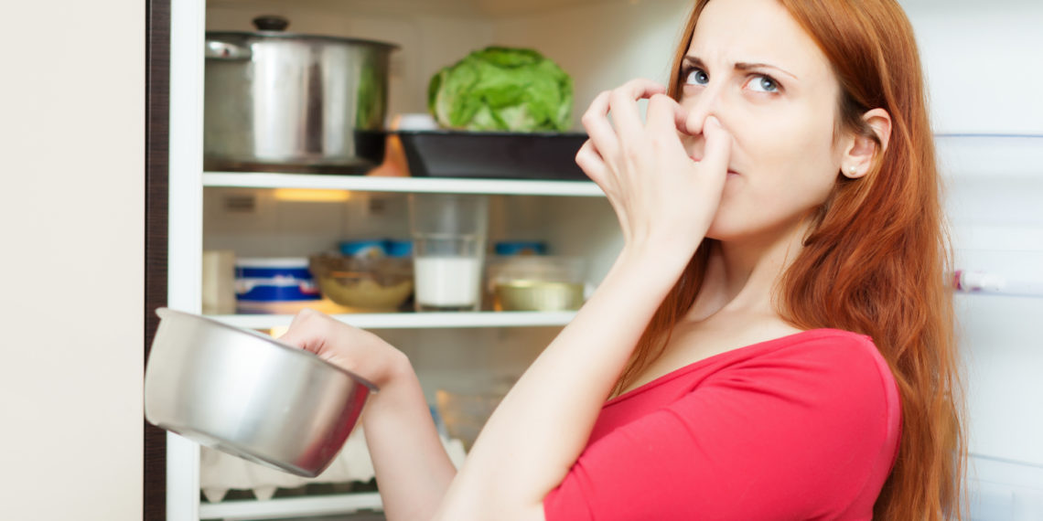 woman in red holding foul food near refrigerator