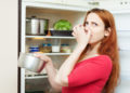 woman in red holding foul food near refrigerator