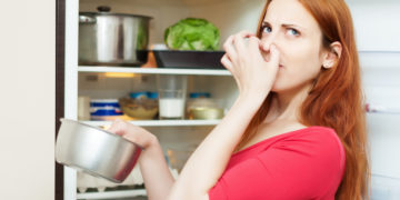 woman in red holding foul food near refrigerator