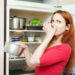 woman in red holding foul food near refrigerator